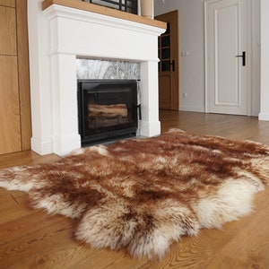 Peut inclure: Un tapis en peau de mouton brun et blanc avec une fourrure longue et douce. Le tapis est posé sur un sol en bois devant une cheminée blanche.