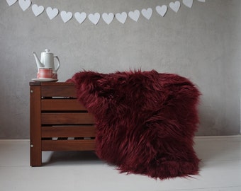 May include: A burgundy faux fur throw draped over a wooden storage bench. A white teapot and two cups are on the bench.