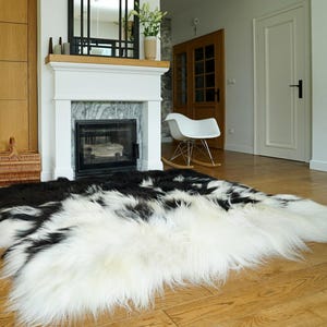 May include: A large, rectangular sheepskin rug featuring a long-pile texture with a high-contrast pattern of black and white patches. The rug is positioned on a light-colored wooden floor, displaying a thick, soft, and shaggy appearance throughout.
