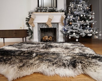 May include: A large, rectangular area rug featuring a long-pile, faux fur texture with a variegated pattern of black, charcoal gray, and cream white fibers. The rug has an irregular, organic shape along its edges, mimicking a natural animal hide.
