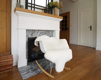May include: A white rocking chair with a curved seat and thin metal legs attached to light wood rockers. A thick, fluffy white sheepskin rug is draped over the seat and backrest of the chair, covering the entire seating area with soft texture.