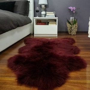 Op de afbeelding: Een diep bordeauxrood nep bontkleed met lange, zachte vezels. Het kleed ligt op een houten vloer in een slaapkamer.