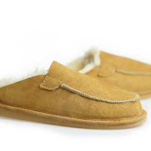 May include: A pair of brown suede slippers with a faux fur lining. The slippers have a simple design with a single seam around the top edge.