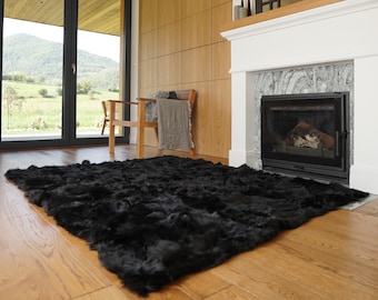 May include: A rectangular black rug with a thick, shaggy, and textured pile surface. The rug features a dense, uniform black color throughout its entire construction, providing a deep and consistent appearance across the floor covering.