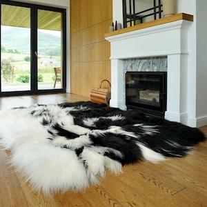 May include: A large, rectangular area rug made of long-haired sheepskin featuring a bold, high-contrast pattern of solid black and white sections. The thick, shaggy texture of the natural fur creates a soft, layered appearance across the floor.
