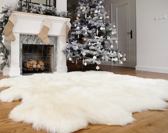 May include: A large, plush, off-white faux fur rug with an irregular, organic shape. The rug features a thick, soft pile texture and is laid out flat on a wooden floor, covering a significant portion of the foreground in a room setting.
