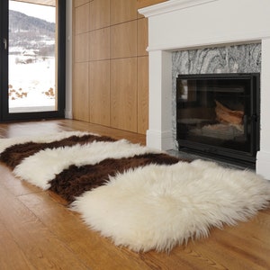 Może przedstawiać: Biało-brązowy dywan ze skóry owczej z długim, puszystym włosiem. Dywan leży na drewnianej podłodze przed kominkiem.