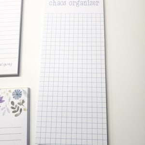 May include: A white notepad with a grid pattern and the text "chaos organizer" printed in purple at the top. The notepad is on a white surface.