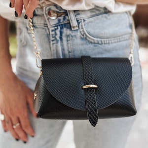 Może przedstawiać: Czarna torebka na ramię z fakturą skóry węża, złotą klamrą i łańcuszkowym paskiem.