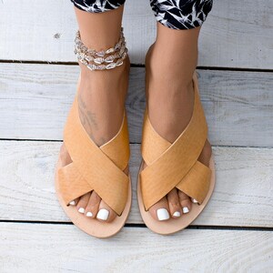 May include: A pair of tan leather sandals with criss-cross straps. The sandals have a simple design and are perfect for summer.