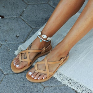 Puede incluir: Un par de sandalias de cuero marr&oacute;n con correas cruzadas. Las sandalias tienen un dise&ntilde;o sencillo y son perfectas para el verano.