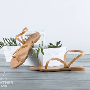 natural tanned leather sandals Syros details of flat leather footbed and straps standing on a basket with olive branch with leaves.
