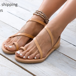 Flat leather sandal in natural veg tanned. Features a simple, smooth two-strap design across the foot and a toe ring. Shows the full profile of the slip-on sandal.