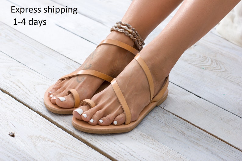 Flat leather sandal in natural veg tanned. Features a simple, smooth two-strap design across the foot and a toe ring. Shows the full profile of the slip-on sandal.