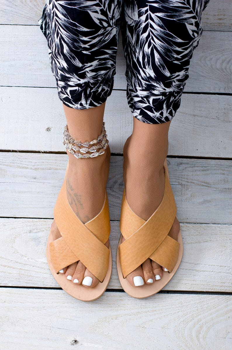 May include: A pair of tan leather sandals with criss-cross straps. The sandals have a simple design and are perfect for summer.