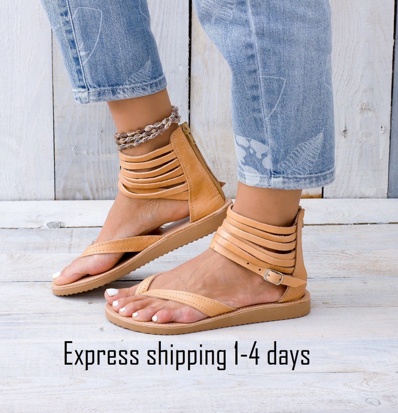May include: Tan leather sandals with multiple straps and a buckle closure. The sandals have a flat sole and a thong style toe.
