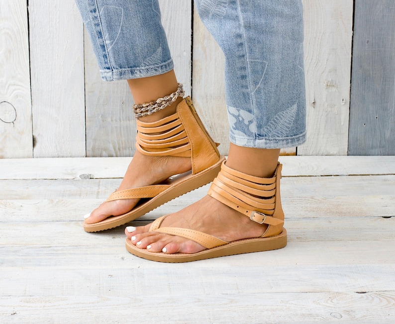 May include: Tan leather sandals with multiple straps and a buckle closure. The sandals have a flat sole and a toe thong.