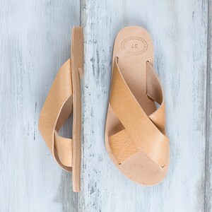May include: A pair of tan leather sandals with a criss-cross strap design. The sandals have a simple, minimalist style and are made of high-quality leather.