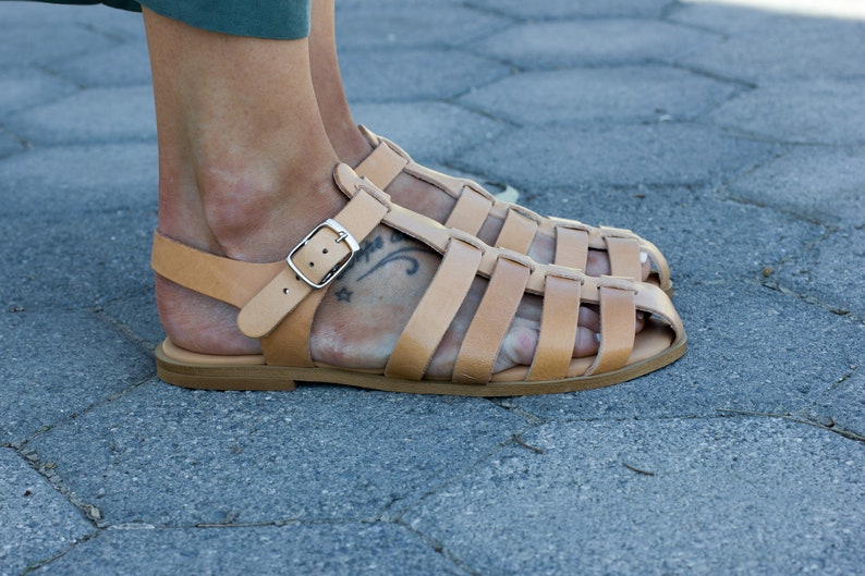 Puede incluir: Sandalias gladiadoras de cuero color marr&oacute;n claro con cierre de hebilla. Las sandalias tienen una suela gruesa y se llevan en los pies.