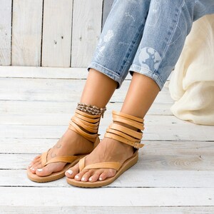 May include: Tan leather sandals with multiple straps wrapping around the ankles. The sandals have a thong style toe strap and a flat sole.