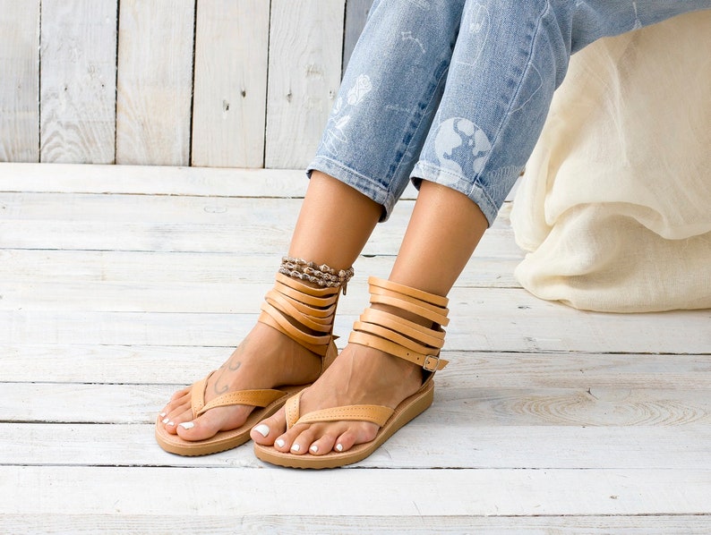 May include: Tan leather sandals with multiple straps wrapping around the ankles. The sandals have a thong style toe strap and a flat sole.
