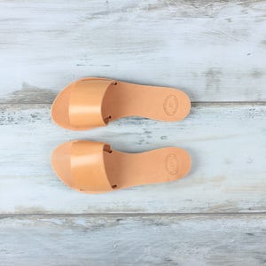 May include: A pair of tan leather sandals with a simple design. The sandals have a flat sole and a strap across the top of the foot.