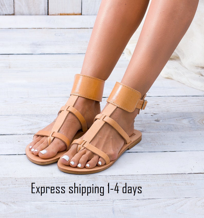 Flat gladiator sandal in natural vegetable-tanned leather. Features multiple minimal straps and a wide ankle cuff with a buckle closure.