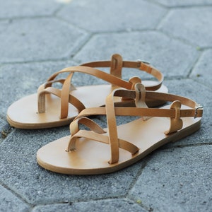 Puede incluir: Un par de sandalias de cuero color marr&oacute;n claro con tiras cruzadas. Las sandalias tienen un dise&ntilde;o sencillo y son perfectas para el clima c&aacute;lido.