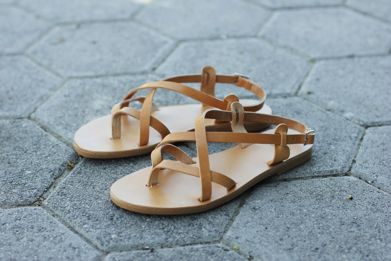 Puede incluir: Un par de sandalias de cuero color marr&oacute;n claro con tiras cruzadas. Las sandalias tienen un dise&ntilde;o sencillo y son perfectas para el clima c&aacute;lido.