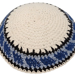 Puede incluir: Una kipá blanca de ganchillo con ribete azul y negro. La kipá es redonda y está hecha de un material suave y texturizado.