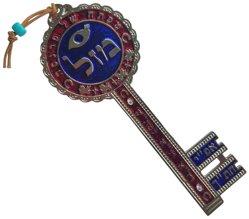 May include: A decorative key pendant with a blue and red design. The key features Hebrew text and a circular emblem. It has a leather cord with a turquoise bead for hanging. The key is made of metal and has intricate details.