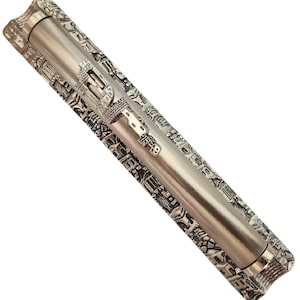 Puede incluir: Un estuche de rollo de Torá de metal plateado con un diseño intrincado de edificios y un pequeño adorno de metal plateado en la parte superior.