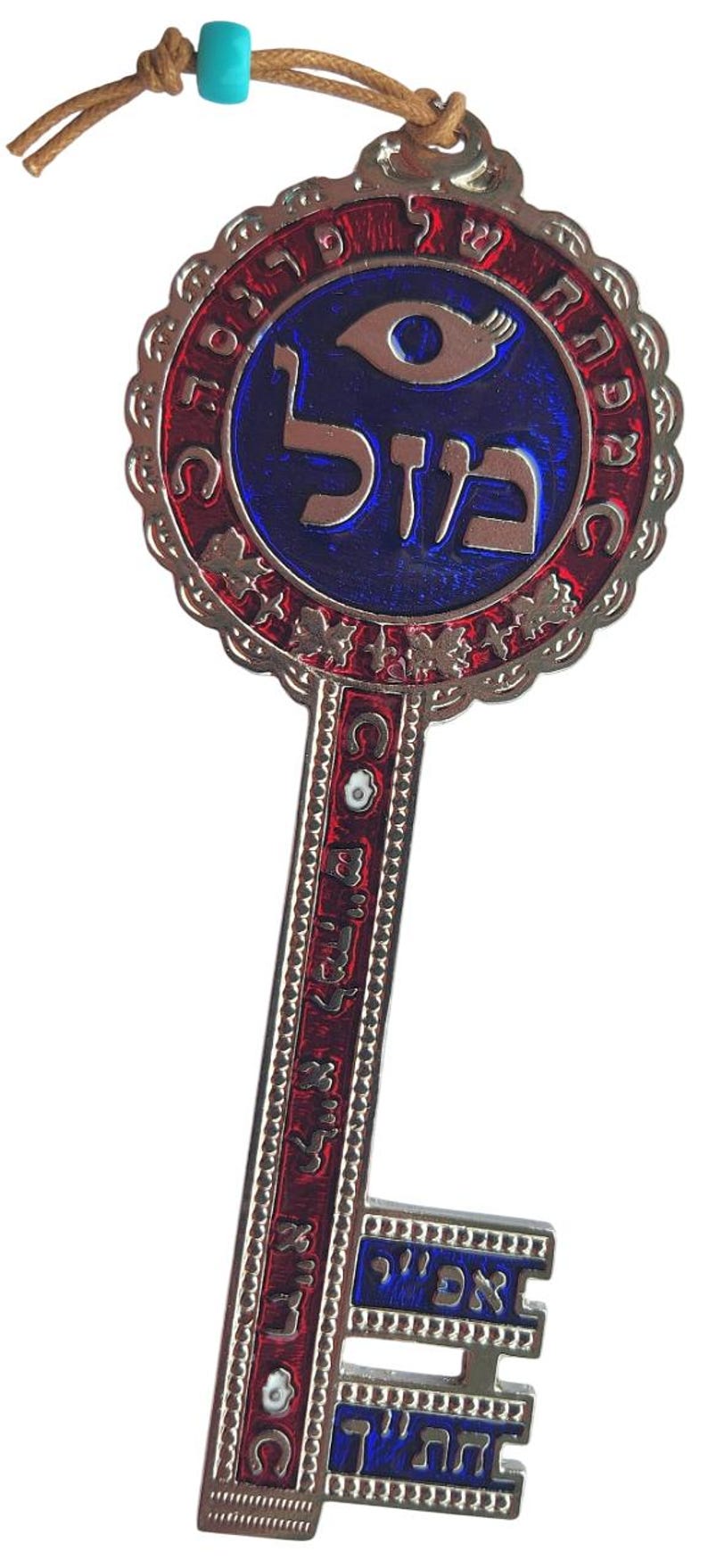 May include: A decorative key pendant with a silver-colored metal frame. The key features red and blue enamel detailing and Hebrew text. A turquoise bead hangs from a brown cord at the top. The key's design includes an eye symbol.