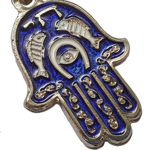 May include: A silver Hamsa hand charm with blue enamel and white details. The charm features a horseshoe, an eye, and two fish. The Hamsa hand is a symbol of protection and good luck.