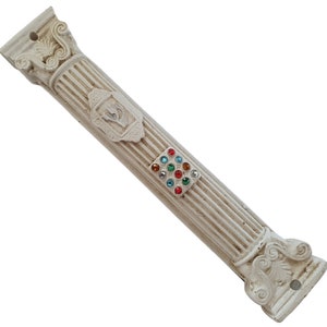 Op de afbeelding: Witte decoratieve mezuzah in de vorm van een kolom met een zilveren Davidster en een vierkant van kleurrijke strass stenen.