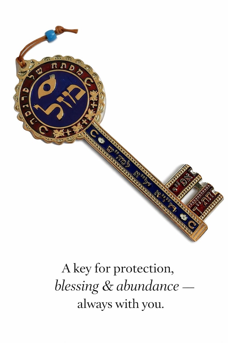 May include: A decorative key with gold-colored metalwork, featuring blue and red enamel accents. The key has Hebrew text and a leather cord with a blue bead. The text on the image reads: "A key for protection, blessing & abundance - always with you."