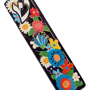 May include: A black mezuzah with a colorful floral design. The mezuzah features a white Hebrew letter "Shin" and a variety of flowers, including daisies, butterflies, and other floral elements.