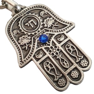 May include: Silver Hamsa hand charm with a blue gemstone and the Hebrew letter 'Chai' inscribed in a circle at the top.