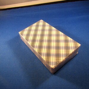 May include: A deck of playing cards in a cardboard box with a plaid pattern in shades of blue, white, and black.