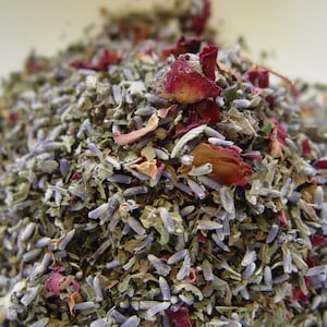 May include: A close-up of a mixture of dried herbs and flowers, including lavender, rose petals, and other botanicals. The mixture is a light green, purple, and pink color.