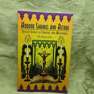 May include: A book titled "Hoodoo Shrines and Altars" with the subtitle "Sacred Spaces in Conjure and Rootwork" is displayed. The cover features a yellow background with a purple border, illustrations of candles, a cross, and an open book.