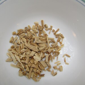 May include: A white bowl filled with light brown wood chips. The chips are small, rectangular pieces, varying in size and shape. The bowl has a green and blue rim.
