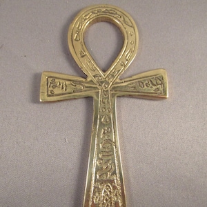 May include: A gold-colored Ankh pendant with intricate details and hieroglyphic symbols. The Ankh is a symbol of life and immortality in ancient Egyptian culture.