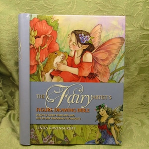 May include: A hardcover book titled "The Fairy Artist's Figure Drawing Bible." The cover features a fairy with butterfly wings, a hamster, and flowers. The book has a light blue spine and is set against a green background.