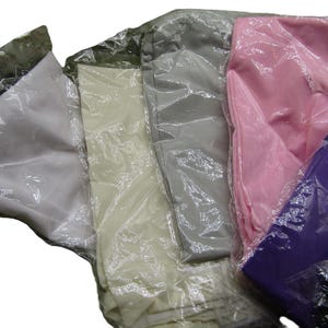 May include: Assortment of folded fabric items in various colors, including white, cream, gray, pink, purple, and black, all individually wrapped in clear plastic. The items appear to be clothing or textiles, neatly packaged for sale.