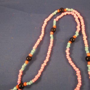 May include: A pink and blue beaded necklace with black beads. The necklace is made of small, round beads and has a simple design.