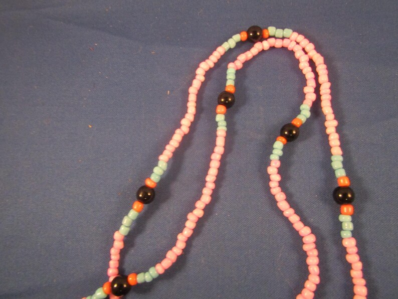 May include: A pink and blue beaded necklace with black beads. The necklace is made of small, round beads and has a simple design.