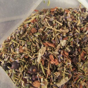 May include: A close-up of a mixture of dried herbs and flowers, including lavender, rosemary, and juniper berries. The mixture is in a clear plastic bag.