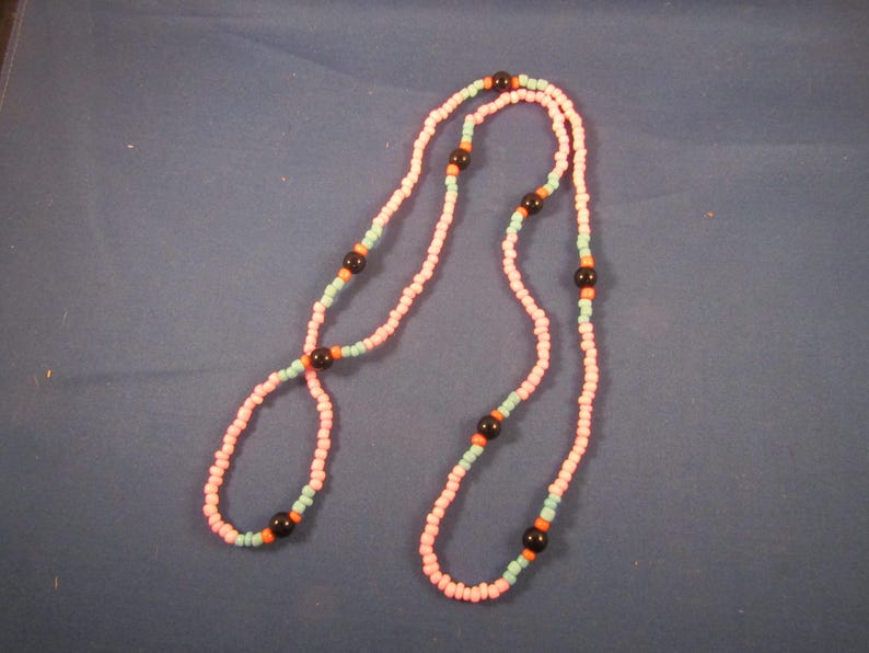 May include: A pink and blue beaded necklace with black beads. The necklace is made of small, round beads and is approximately 76 cm long.