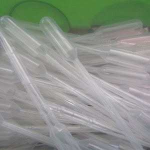 May include: A pile of clear plastic droppers, also known as pipettes, are stacked together. The droppers are used for dispensing small amounts of liquid.